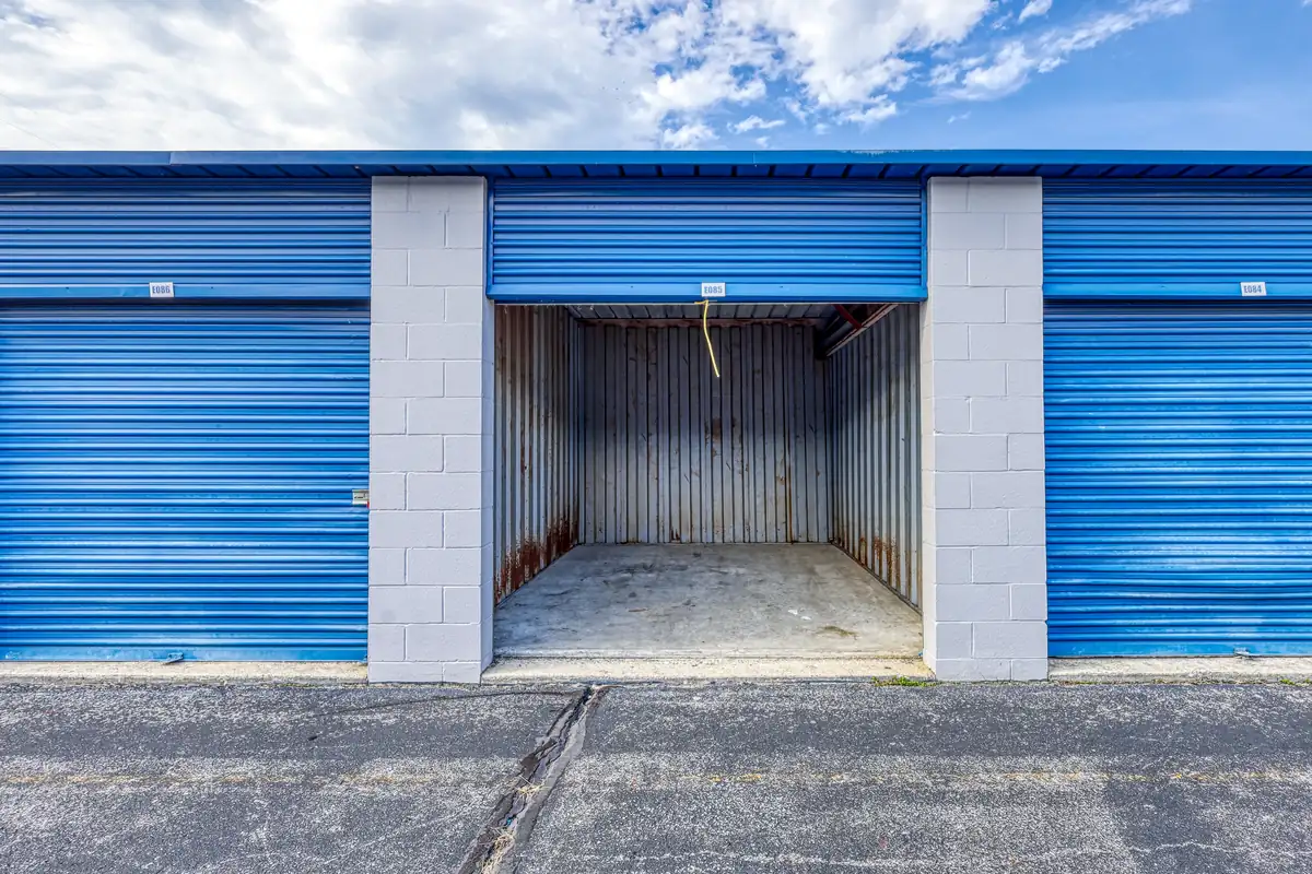 Interior view of an open, empty drive-up storage unit featuring a blue roll-up door and concrete floor.
