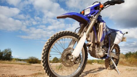 Dirt bike in a dry, flat landscape with shrubs and trees.
