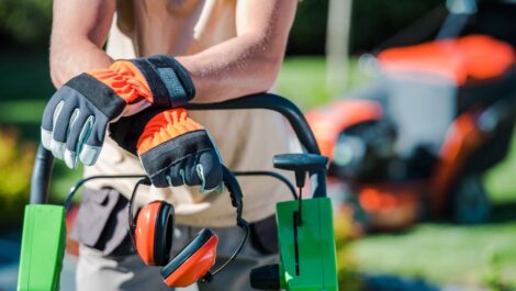 Person with gloves and noise-canceling headphones leaning on a lawn mower.