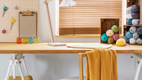 Chair with a yellow blanket at a desk with a lamp and colorful yarns in the workspace interior.