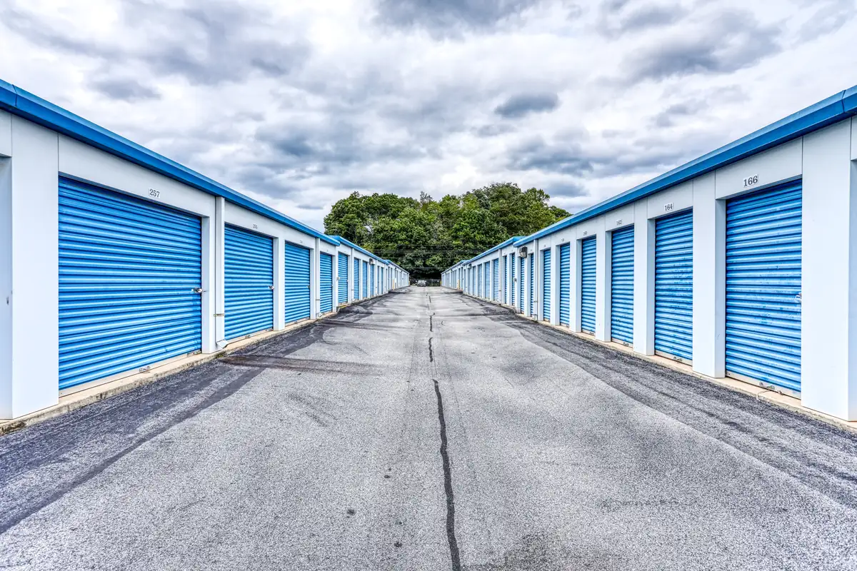 Long row of convenient drive-up storage units with blue roll-up doors and wide paved aisles.
