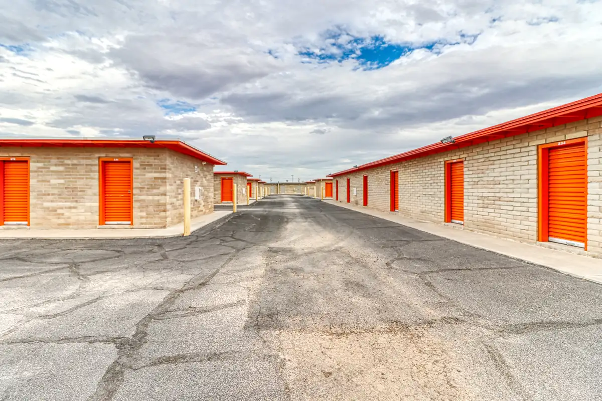 Wide paved drive aisle between rows of orange drive-up storage units in Casa Grande.