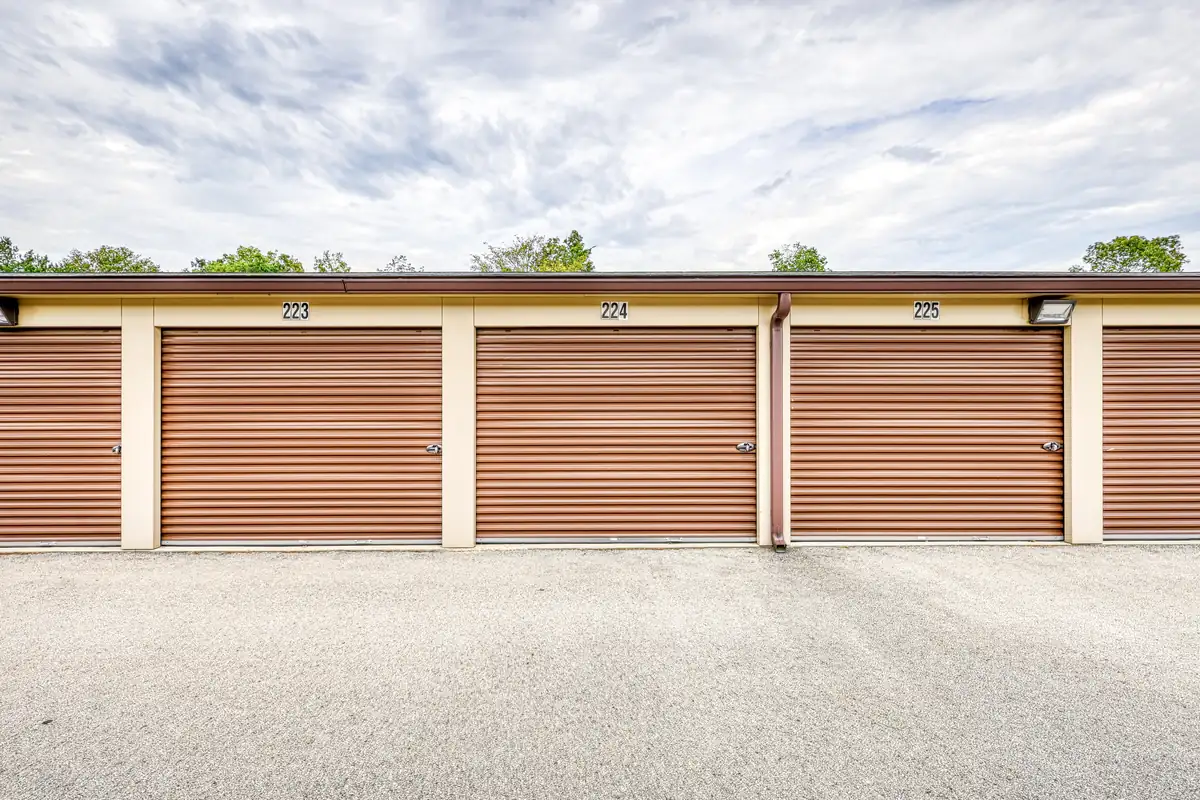 Paved drive aisle facing a row of brown exterior roll-up doors on a tan storage building.