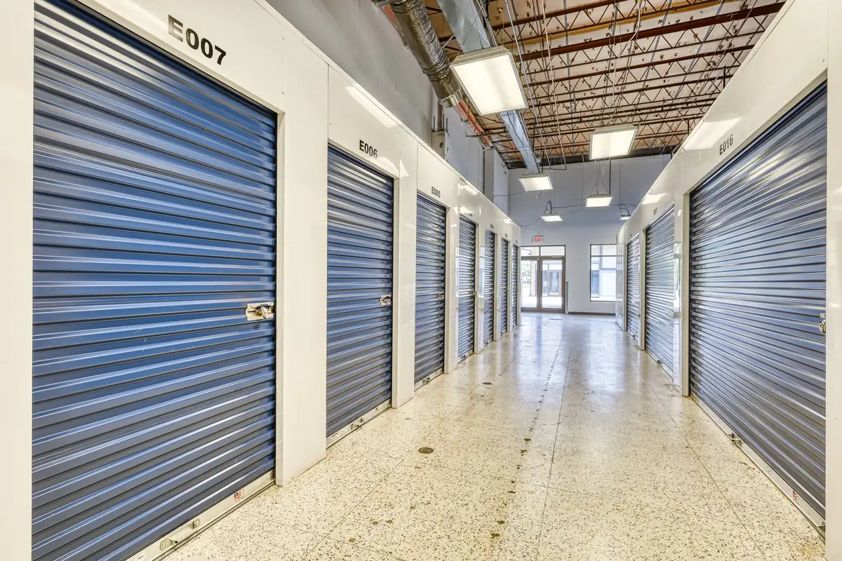 Brightly lit interior hallway with blue doors for climate-controlled storage units.